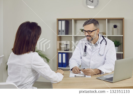 Beautiful, slender, young brunette woman at reception with gray-haired doctor in glasses and white coat. 132351133