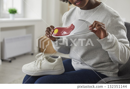 Young African American woman holding orthotic arch support insole for her footwear Young African American woman holding orthotic arch support insole for her footwear 132351144