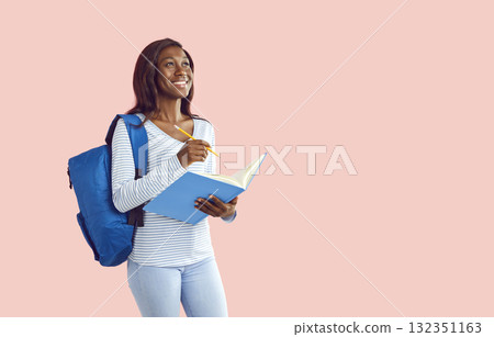 Happy smiling girl holding notebook with backpack and writing on pink background. 132351163