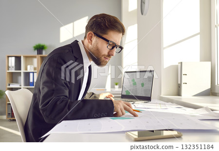 Cadastral surveyor sitting at office desk and working with city plans and cadastral maps Cadastral surveyor sitting at office desk and working with city plans and cadastral maps 132351184