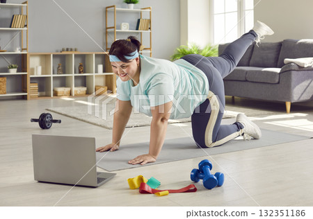 Happy overweight woman using laptop and doing sports workout with remote fitness trainer Happy overweight woman using laptop and doing sports workout with remote fitness trainer 132351186