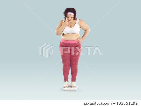 Overweight young woman weighs herself on scales and becomes worried about her weight 132351192