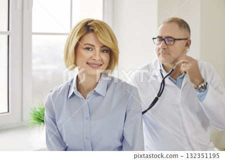 Mature patient in clinic for checkup. Doctor with stethoscope examining woman's lungs and heartbeat 132351195