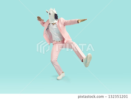 Funny man in horse mask and pink party suit dancing in studio with blue background 132351201
