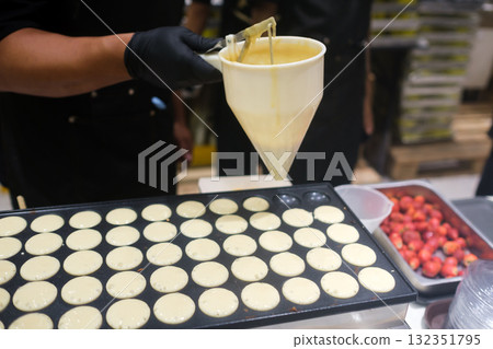 Pancake batter is poured into a frying pan in a busy kitchen at a food market. 132351795