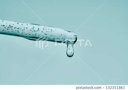 The texture of a serum with bubbles dripping from a pipette on a mint background. The texture of a serum with bubbles dripping from a pipette on a mint background. 132351861