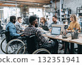 Smiling employees in wheelchairs chat with colleagues in a modern office. A group of young people with disabilities use a laptop and computer in a positive work environment 132351941