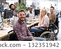 Smiling employees in wheelchairs chat with colleagues in a modern office. A group of young people with disabilities use a laptop and computer in a positive work environment 132351942