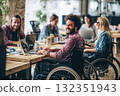 Smiling employees in wheelchairs chat with colleagues in a modern office. A group of young people with disabilities use a laptop and computer in a positive work environment 132351943