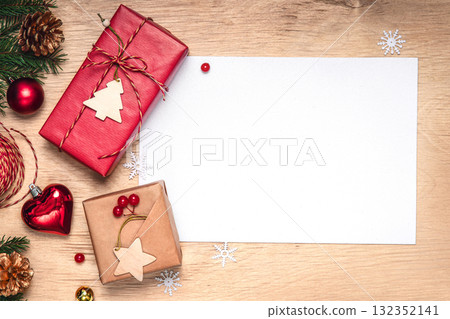 Christmas flat lay background: kraft wrapped gifts with wooden tags, twine and packing supplies on a wooden table. Blank white card for text. Ideal for greetings and New Year goals 132352141