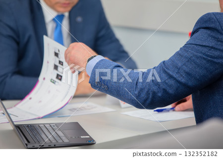 Unrecognizable businessmen in suits and ties at a desk leafing through paper catalogs. Concept of discussion and negotiations. Unrecognizable businessmen in suits and ties at a desk leafing through paper catalogs. Concept of discussion and negotiations. 132352182
