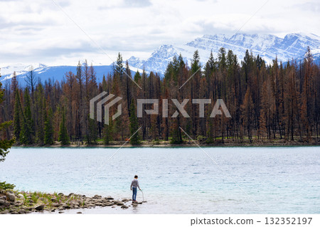 Teen hiker at the lake among mountain peaks and burnt forest. 132352197