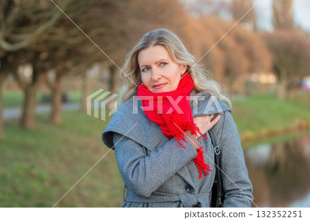 Beautiful adult blonde woman in a gray coat walks in the park. Thoughtful woman fifty years old. Beautiful adult blonde woman in a gray coat walks in the park. Thoughtful woman fifty years old. 132352251