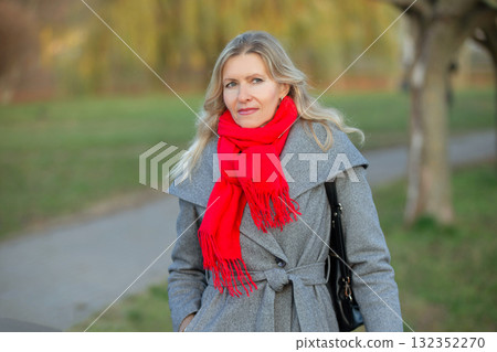 Beautiful adult blonde woman in a gray coat walks in the park. Thoughtful woman fifty years old. 132352270