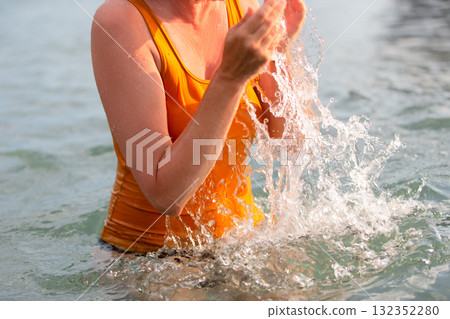 The hands of an unrecognizable woman in a yellow T-shirt splash sea water. 132352280