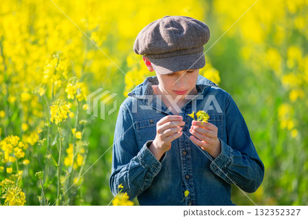 A village boy in a denim shirt and a vintage cap in a rapeseed yellow field. A village boy in a denim shirt and a vintage cap in a rapeseed yellow field. 132352327