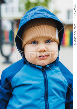 A little boy in overalls runs on the street. A child in a raincoat walks in the yard. Children's overalls are mudproof 132352502