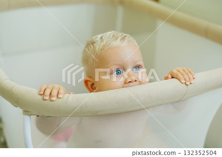 A little boy in a diaper sits in a playpen. A playpen for children. 132352504