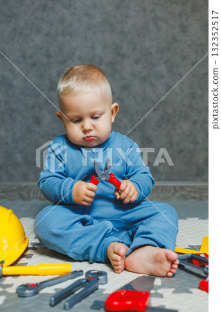 Boy 1 year old in a blue romper plays with toys at home in the living room. Child self-development. Toys for babies. 132352517