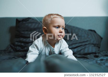 Child in bed. Cute toddler boy in white blouse and pants laughing while sitting in bed. 2 year old boy playing while sitting in bed. Home clothes for boys. Child in bed. Cute toddler boy in white blouse and pants laughing while sitting in bed. 2 year old boy playing while sitting in bed. Home clothes for boys. 132352527
