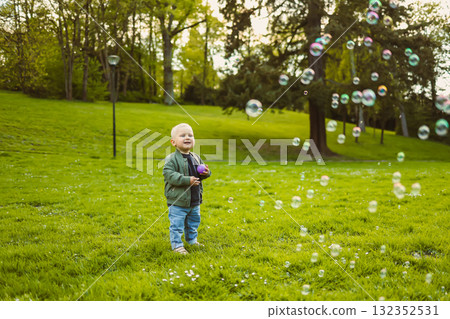 Little 2 year old boy running on green grass with soap bubbles. Toddler boy enjoying a walk in nature. Child having fun in city park. Little 2 year old boy running on green grass with soap bubbles. Toddler boy enjoying a walk in nature. Child having fun in city park. 132352531