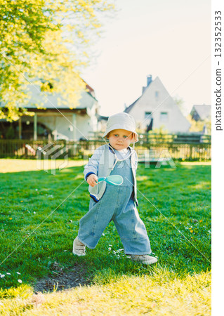 Cute boy running on the grass in a stylish shirt and sunbathing in the sun. Carefree childhood with joyful laughter of a child. Toddler having fun and enjoying a walk in nature. 132352533