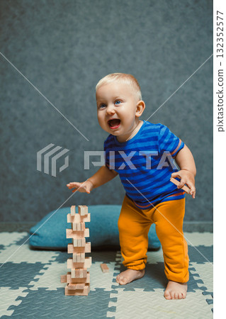 A one-year-old boy at home in a t-shirt and pants is playing in the room. The child is having fun playing on his own. A one-year-old boy at home in a t-shirt and pants is playing in the room. The child is having fun playing on his own. 132352577
