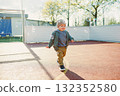 Toddler boy running outside with soap bubbles. Child on a warm spring day for a walk in a jacket and hat. 132352580