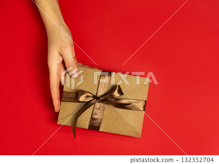 A female hand holding an envelope with a satin ribbon on a red background A female hand holding an envelope with a satin ribbon on a red background 132352704