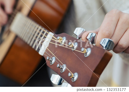 Close up of hands of a young woman tuning guitar. Tuning new six-stringed acoustic guitar to make it sound right 132353177