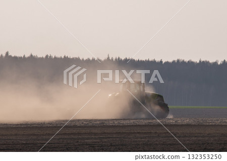 Tractor plowing farm land in spring. Tractor working on field, cultivating ground, dust covering rear part of tractor, plowing field for growing some grain or vegetables Tractor plowing farm land in spring. Tractor working on field, cultivating ground, dust covering rear part of tractor, plowing field for growing some grain or vegetables 132353250