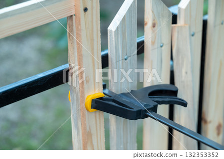 Building wooden fence DIY. Attaching wooden planks with same distance to make even fence using building bracket Building wooden fence DIY. Attaching wooden planks with same distance to make even fence using building bracket 132353352