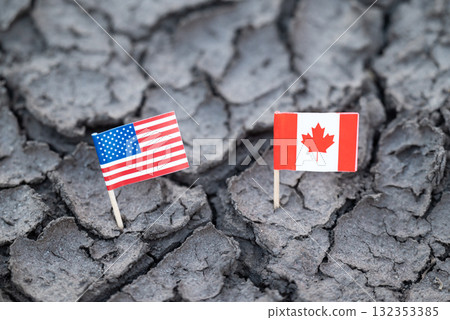 USA and Canada flags on cracked dry earth. Small American and Canadian flags placed in arid, cracked soil, symbolizing political crisis and international problems of countries USA and Canada flags on cracked dry earth. Small American and Canadian flags placed in arid, cracked soil, symbolizing political crisis and international problems of countries 132353385