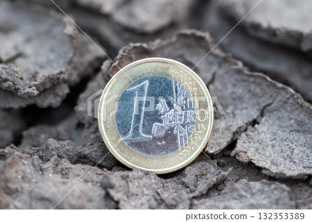 1 euro coin lying in cracked dry earth. A single euro coin resting in cracked, dry ground, symbolizing economic tension, instability in Europe 132353389