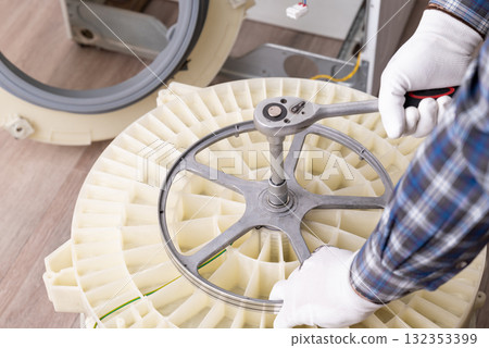 Repairing a washing machine with tools in a service workshop. A technician uses a wrench to fix a washing machine in a service workshop, focusing on the drum assembly 132353399