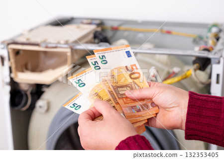 Counting euro cash near washing machine during repair work. Hands are holding money while a washing machine is being repaired nearby, financial transaction for washer service Counting euro cash near washing machine during repair work. Hands are holding money while a washing machine is being repaired nearby, financial transaction for washer service 132353405