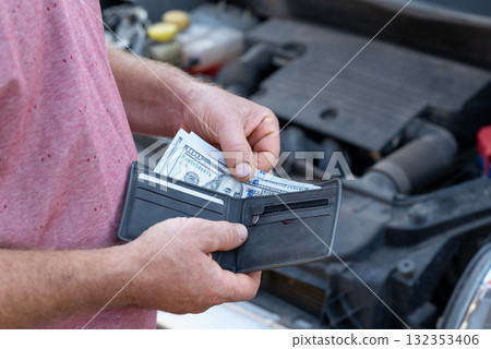 Driver car owner taking money from its wallet on the background of open car hood. Paying for repairing car, price for fixing broken down vehicle 132353406