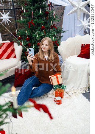 Happy blonde woman taking selfie with Christmas gift by festive tree 132353547