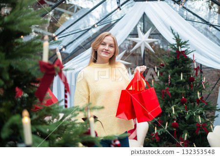 Smiling blonde woman holding red shopping bags near Christmas tree Smiling blonde woman holding red shopping bags near Christmas tree 132353548