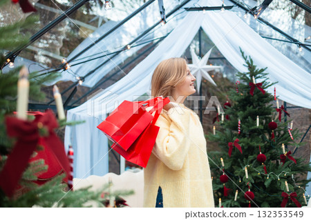 Smiling blonde woman holding red shopping bags near Christmas tree Smiling blonde woman holding red shopping bags near Christmas tree 132353549