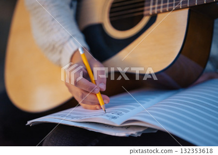 Woman's hand writing notes in her notebook while playing the guitar, close up. Concept of making music, practicing on an instrument and getting the musical education Woman's hand writing notes in her notebook while playing the guitar, close up. Concept of making music, practicing on an instrument and getting the musical education 132353618