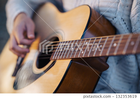 Guitar in girls hands, playing music, close up. Young female guitarist in white sweater practicing instrument outdoors 132353619