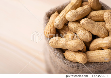 Bag with peanuts on wooden background. Close up of unpeeled peanuts, harvest of nuts 132353695