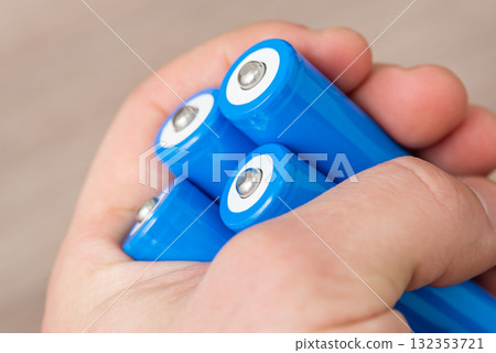 Hand of a man holding four blue 18650 batteries in hand. Using modern high capacity rechargeable accumulators Hand of a man holding four blue 18650 batteries in hand. Using modern high capacity rechargeable accumulators 132353721