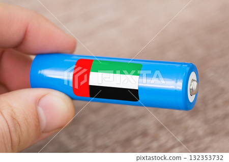 Rechargeable battery with flag of United Arab Emirates in hand of a man. Production of batteries in UAE concept Rechargeable battery with flag of United Arab Emirates in hand of a man. Production of batteries in UAE concept 132353732