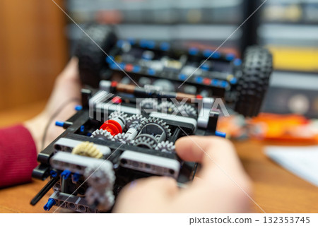 Complex mechanism of a toy car made by a boy in his hands. Little boy playing with engineering set for making different machines Complex mechanism of a toy car made by a boy in his hands. Little boy playing with engineering set for making different machines 132353745