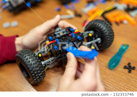 Close up of part of car in hands of a boy. Kid makes a car using parts of engineering mechanics constructor set Close up of part of car in hands of a boy. Kid makes a car using parts of engineering mechanics constructor set 132353746