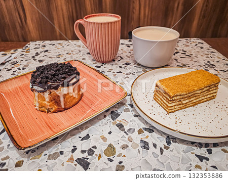 Close-up of two cups of coffee served with a cinnamon bun (Cinnabon) and a honey cake (Medovik) from a side view. Perfect for breakfast, cozy lifestyle, and dessert photography concepts. Close-up of two cups of coffee served with a cinnamon bun (Cinnabon) and a honey cake (Medovik) from a side view. Perfect for breakfast, cozy lifestyle, and dessert photography concepts. 132353886