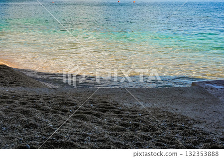 Close-up view of sand along the shore with clear water of the sea. Natural beach texture and tranquil coastal scenery, suitable as a background or texture. 132353888