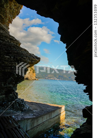 Natural cave opening on the Budva coast showing the Adriatic Sea and distant Hawaii Island. Coastal and rocky landscape. Natural cave opening on the Budva coast showing the Adriatic Sea and distant Hawaii Island. Coastal and rocky landscape. 132353899